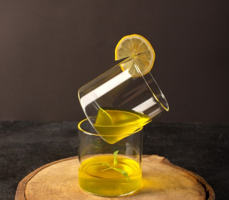 front-view-glasses-with-juice-lemon-juice-inside-transparent-glasses-along-with-flowers-brown-wooden-desk-grey-background-cocktail-lemon-drink_140725-18200